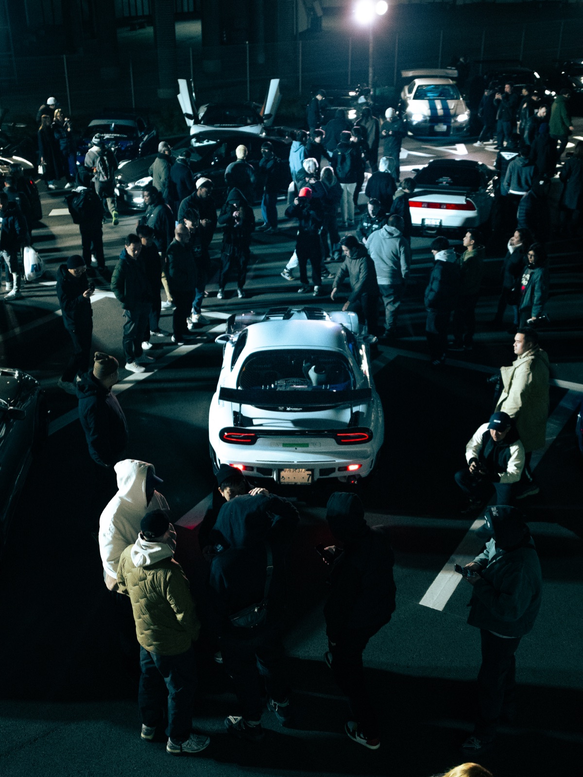 Reunión nocturna de autos con un Mazda RX-7 blanco al centro